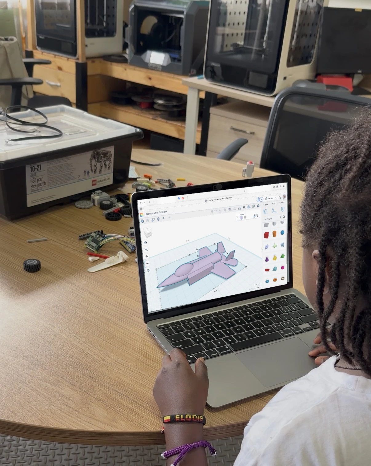 A young learner designing a jet aircraft in 3D on a laptop, with robotics parts and 3D printers in the AeRoCAD lab